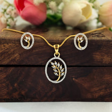 Gold leaf pendant necklace with matching stud earrings, displayed on a dark wooden box with blurred pink and white flowers in the background.