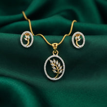 Gold jewelry set with a pendant necklace and matching earrings, featuring a leaf motif set in a circular frame with clear stones, displayed on a draped dark green satin fabric.
