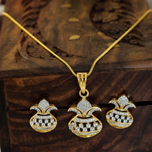 Gold-tone jewelry set with a pendant necklace and two matching earrings, each featuring a gold pouch-like charm set with clear stones, displayed on a carved wooden box with blurred pink and white flowers in the background.