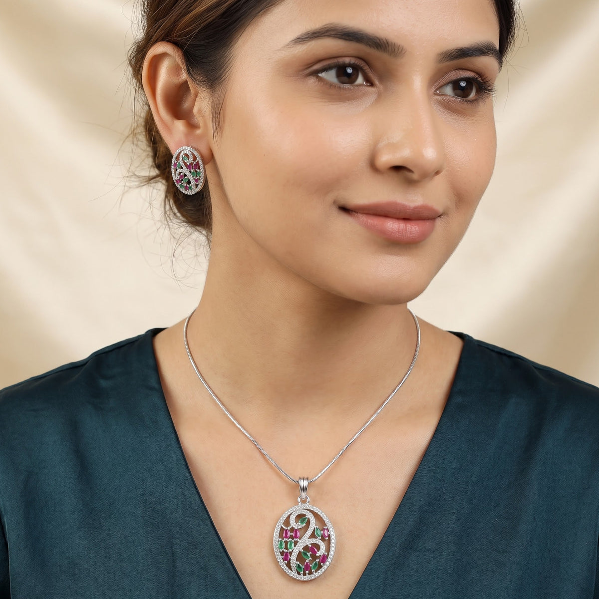 A woman wearing a silver-toned oval pendant necklace and matching stud earring. The jewelry features a central pink and green floral motif with a white circular background and a small red accent.